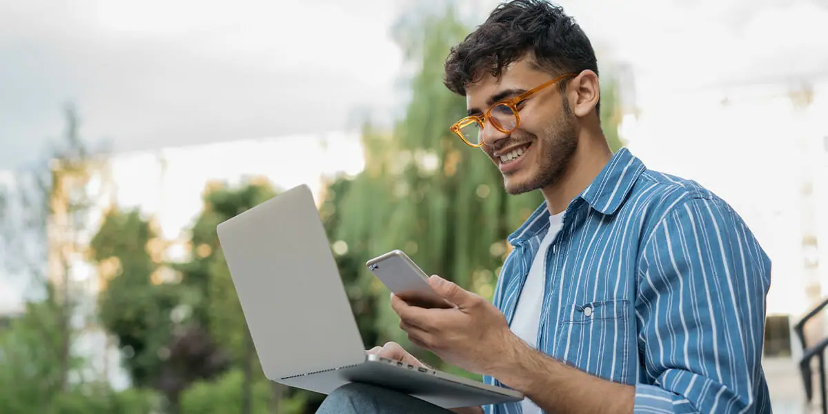 A man with orange glasses multitasking with a phone and a computer